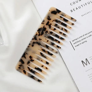 Detail of wide-tooth acetate hair comb with marble pattern on white silk and magazine