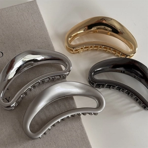 Detail view of large metal moon-shaped hair claws in gold, silver, grey, and black