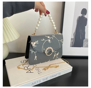 Detail of grey crossbody bag featuring floral embroidery and large pearl handle