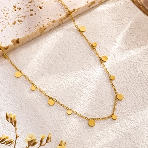Minimalist gold choker necklace with small circular disks on textured white stone