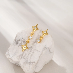 Macro shot of gold S925 silver star earrings with clear zircons on white marble