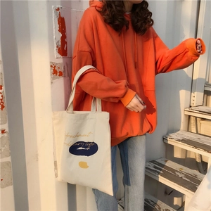Outdoor shot of a canvas shoulder bag with Refreshment text and orange sweatshirt
