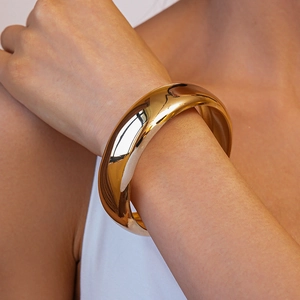 Close-up of a chunky wide gold-plated bangle with a high-polished mirror finish