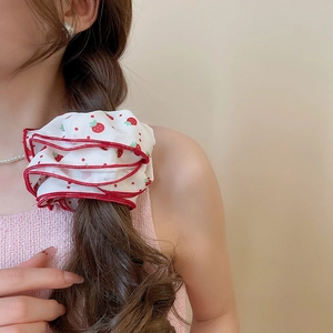 Detail of white fabric scrunchie with red strawberry print and wavy edge on a ponytail