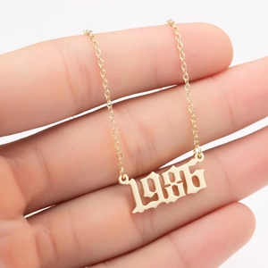 Close-up of gold 1986 year pendant necklace with delicate link chain held in hand