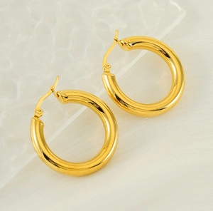 Macro shot of 18K gold hollow hoop earrings on white silk and glass background