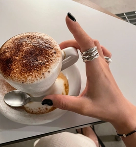 Close-up of triple-layer wavy 925 sterling silver ring worn by a model in a cafe