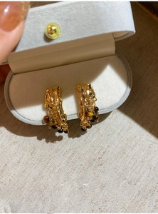 Close-up of golden irregular lava texture earrings with hanging brown resin beads