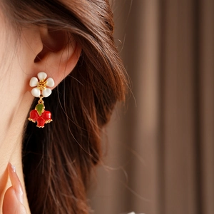 Close-up of vintage flower and red berry drop earrings worn by a model on a brown background
