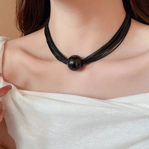 Detail view of multi-layered black chain necklace featuring a large round metal ball pendant