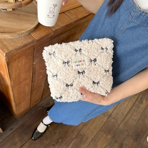 Detail of cream sherpa makeup bag with black bow pattern and embroidered brand label