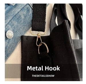 Detail of gold-tone spring hook and D-ring on black canvas tote bag with woven strap