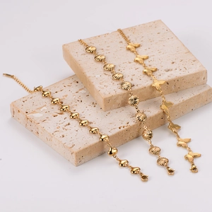 Three gold stainless steel bracelets with heart, butterfly and bead charms on stone base