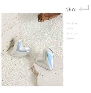 Close-up of silver heart stud earrings placed on white textured stone and wooden block