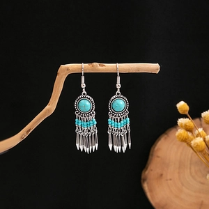 Macro detail of Bohemian turquoise earrings with beads and metallic tassel on wood