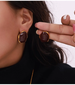 Detailed view of deep brown enamel stud earrings with gold metal frame on model