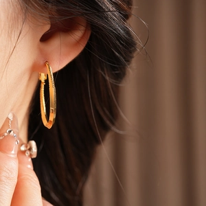 Close-up of a model wearing large golden hoop earrings with elegant twisted texture design