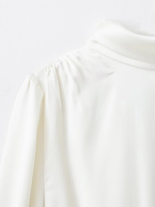 Détail du chemisier en satin blanc avec col montant et plis élégants aux épaules