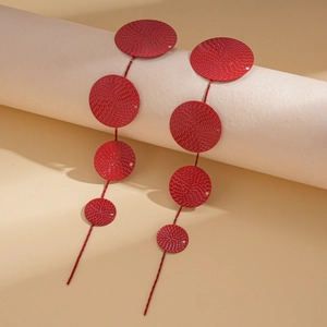Close-up of red metal disk tassel earrings featuring intricate woven textures and long silhouette