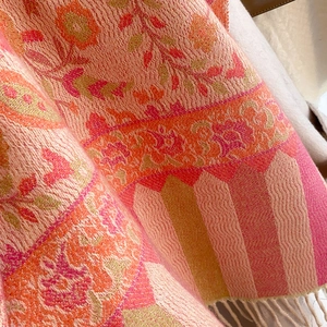 Close-up detail of ethnic floral patterns and tassel fringe on a warm woven shawl scarf