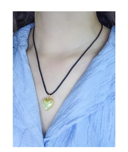 Close-up of minimalist gold heart pendant on thin black cord necklace worn on neck