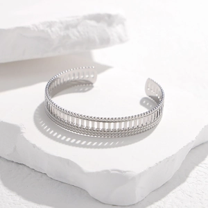 Detail of silver hollow cuff bracelet with beaded edges on white stone backdrop