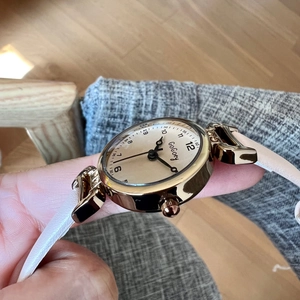 Detail of female wristwatch with gold case and white leather strap on a natural background