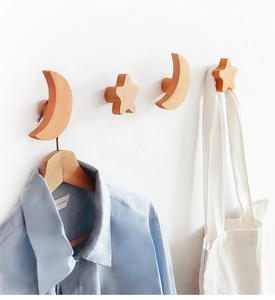 Star and moon solid wood wall hooks shown holding a shirt and canvas bag on white wall