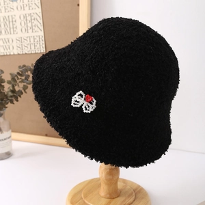Detalle del sombrero bucket negro de felpa con lazo de perlas y botón de corazón