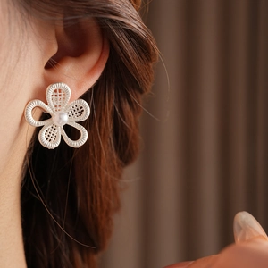 Détail de boucles d'oreilles fleurs évidées en argent avec perle portées par un mannequin
