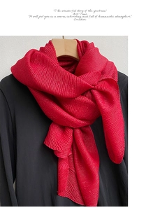 Dettaglio della sciarpa plissettata rossa drappeggiata su un cappotto nero su gruccia