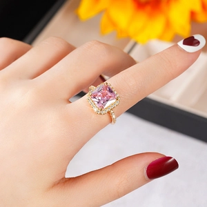 Macro detail of a gold ring featuring a large pink square gemstone with a pavé halo