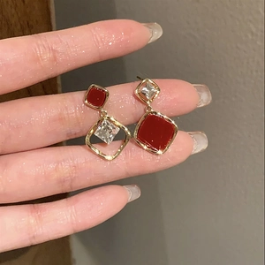 Detail of asymmetric gold earrings with burgundy enamel and clear zircon stones