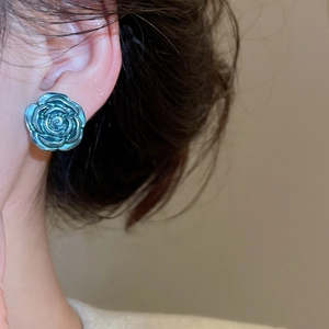 Detailed view of iridescent blue-green 3D rose earrings on model with metallic finish