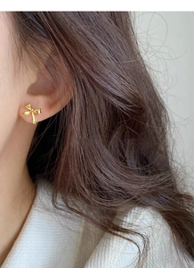 Detailed view of elegant gold bow stud earrings worn by a model in a minimalist style