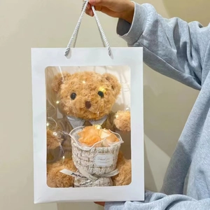 Close-up of brown teddy bear with fabric flower bouquet in a white gift bag with LED lights