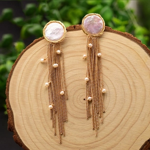 Detailed view of baroque pearl earrings with gold metal tassels on natural wood