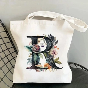 White canvas tote bag featuring a vintage floral letter R print on a metal chair