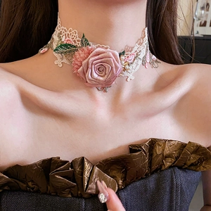 Detailed view of pink fabric rose and green leaf embroidery on white lace choker necklace