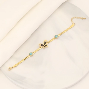 Golden butterfly bracelet with turquoise beads and black inlay on white marble surface