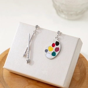 Detail of asymmetric brush and colorful palette earrings on a white gift box display