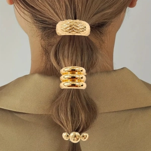Detail of three golden geometric hair ties with textured rhombus and wave designs