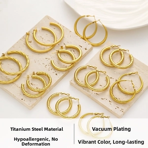Detail of gold-plated titanium hoop earrings with diverse textures on beige travertine