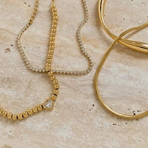 Set collana con cuore di perle dorate e bracciale rigido su base di marmo beige