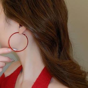 Close-up of a model wearing large glossy red hoop earrings with a minimalist design