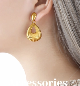 Detail of golden teardrop earrings featuring intricate shell-like textures on a model