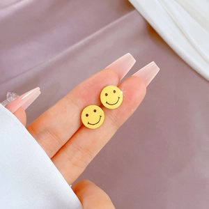 Minimalist golden titanium steel smiley face stud earrings shown on fingertip for scale