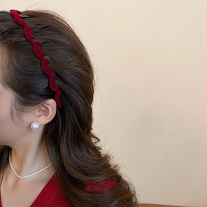 Detail view of a vintage red flocked wavy headband paired with elegant pearl jewelry on model