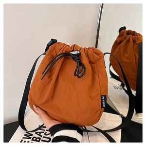 Detail view of orange drawstring bucket bag with nylon texture and black shoulder strap