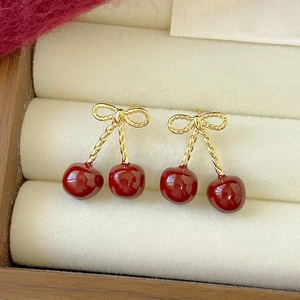 Elegant resin cherry earrings with golden bow studs on beige velvet jewelry display